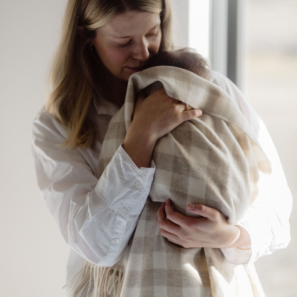 Woman holding a baby wrapped in a blanket in a softly lit room.