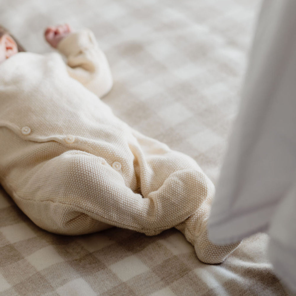 Baby in a white onesie lying on a checkered blanket
