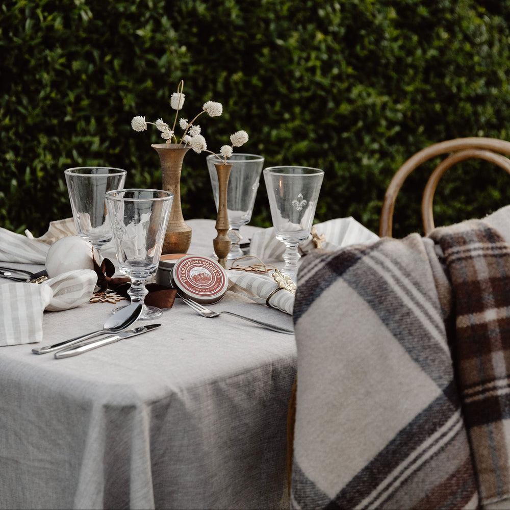 Set table with plaid blanket and floral arrangement against a green hedge background
