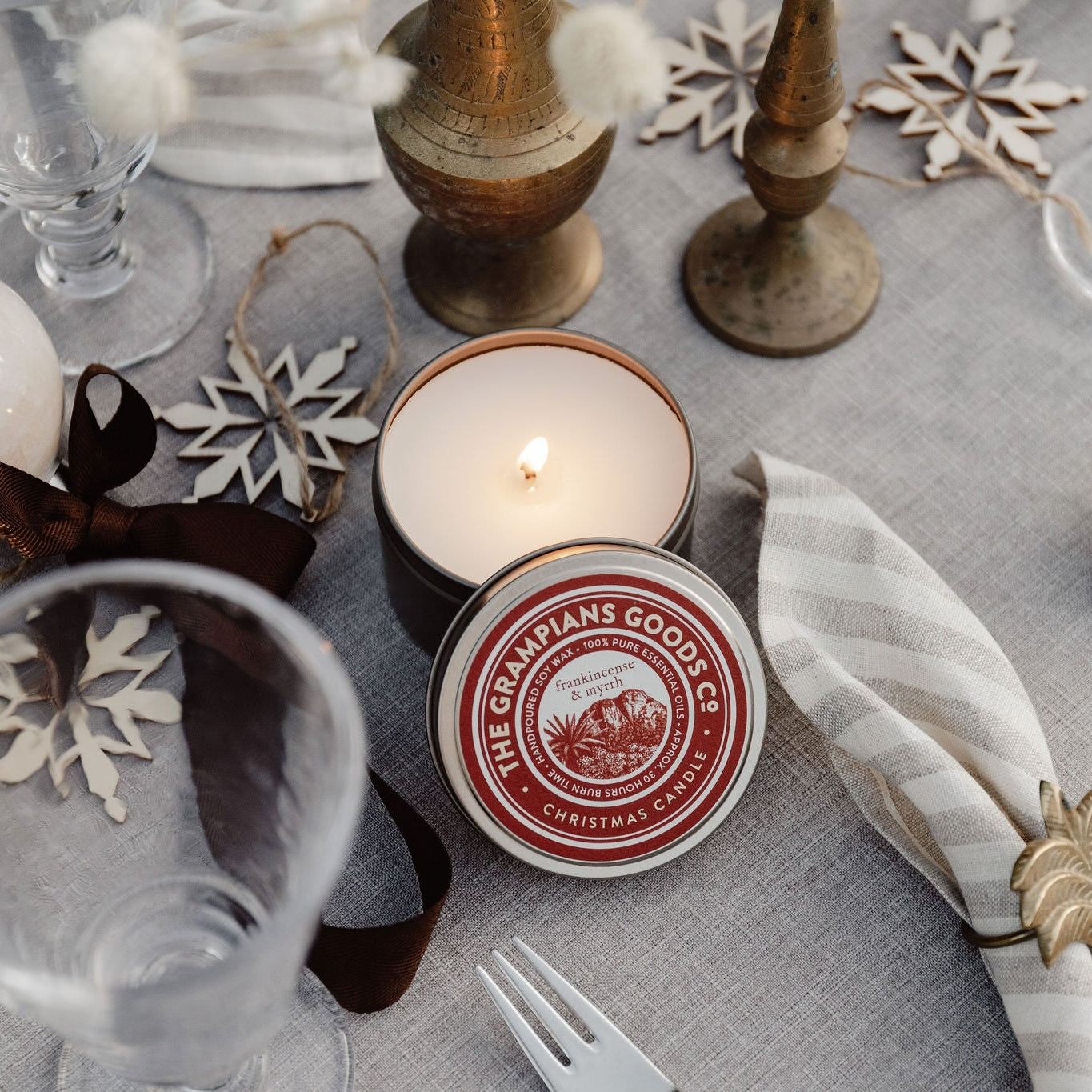 Table setting with candles, glasses, and decorative items on a gray tablecloth.
