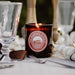 Candle with 'The Grampians Goods Co' label on a table setting with glasses and flowers.