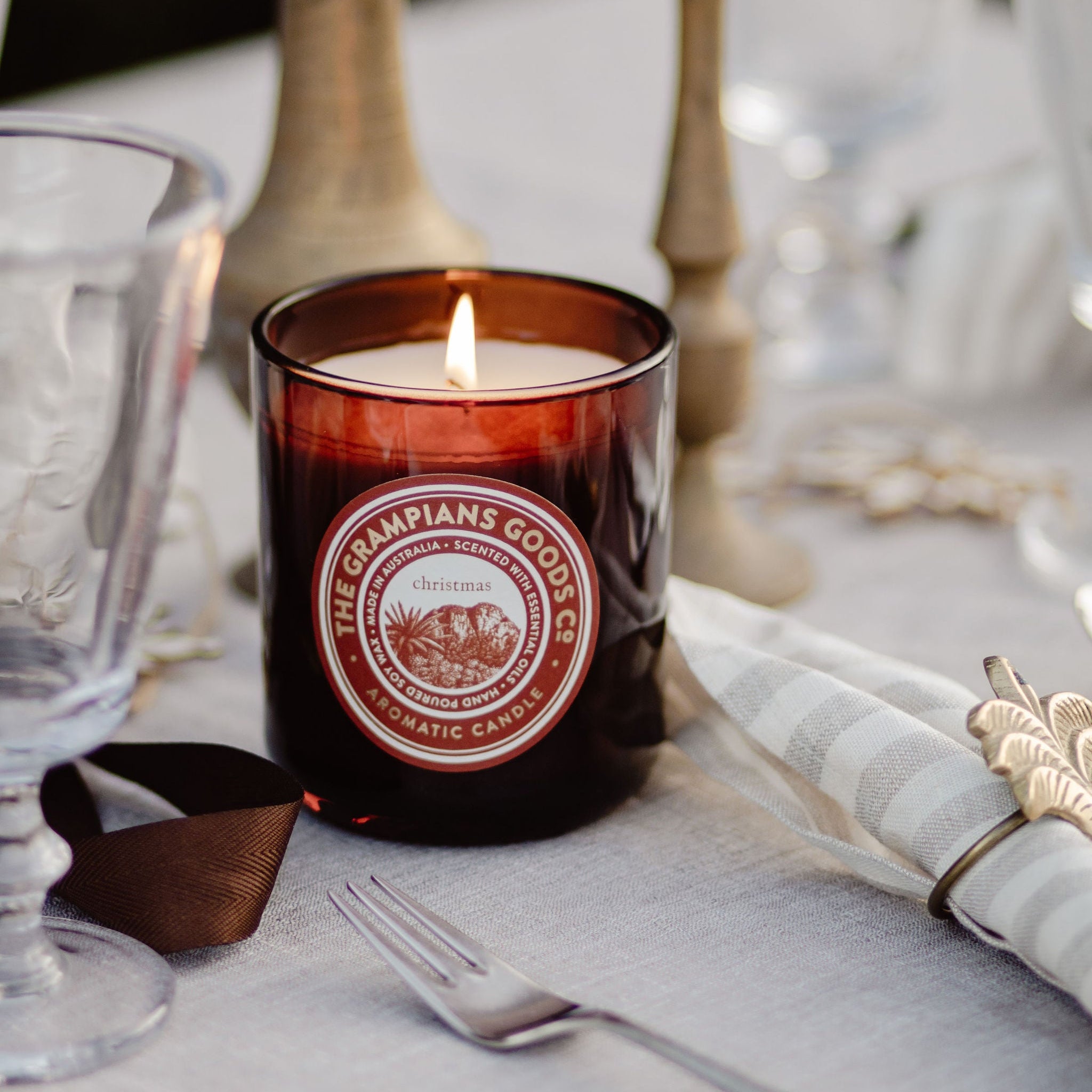 Candle with a label on a table setting with glasses and napkins.