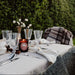 Outdoor table setting with glasses, candle, and plaid blanket against a green hedge background