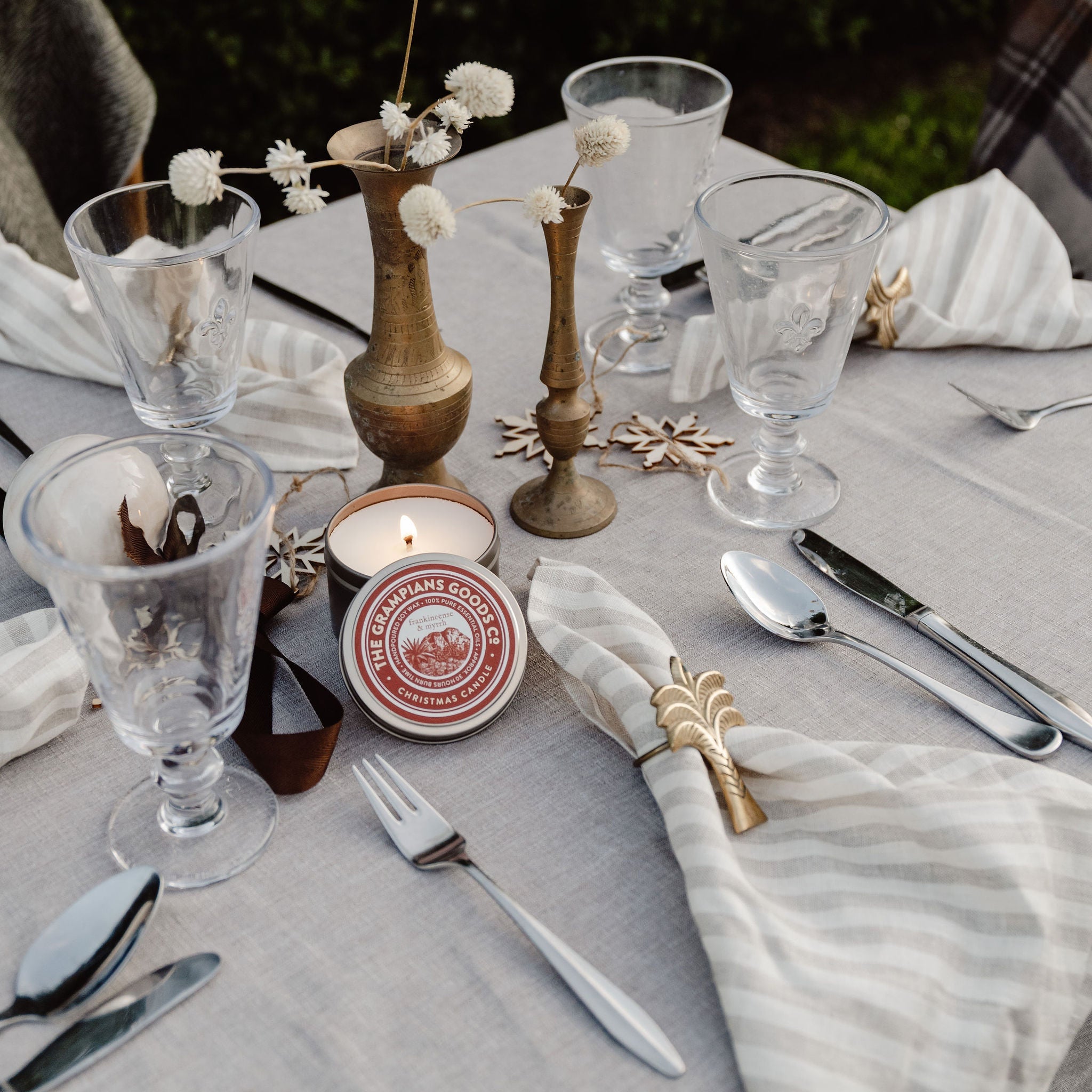 Dining table setting with candles, glasses, and cutlery on a white tablecloth.
