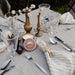 Dining table setting with candles, glasses, and cutlery on a white tablecloth.