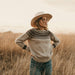 Woman wearing a patterned sweater and hat standing in a field with a neutral background