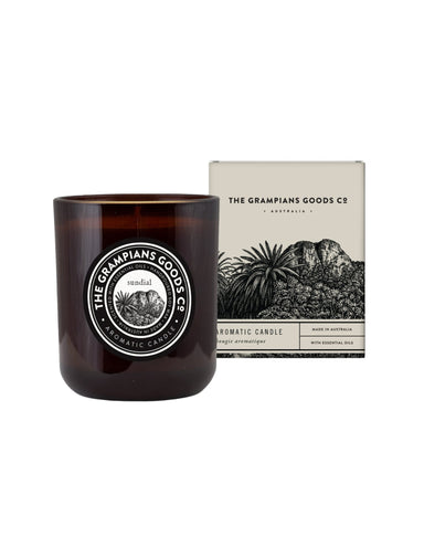 An amber glass scented candle in a cylindrical jar with a white circular label, standing next to its cream-colored product box featuring black botanical illustrations. The brand 'The Grampians Goods Co' is clearly visible on both the jar label and the box.