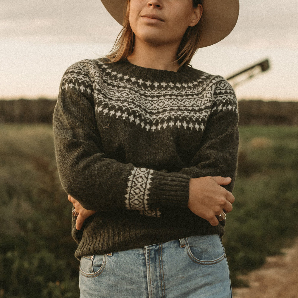 Woman wearing a patterned sweater and wide-brimmed hat standing in a field.