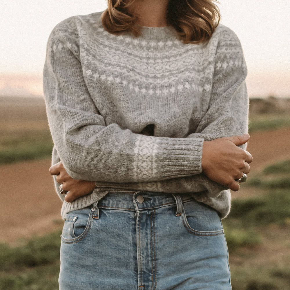 Person wearing a patterned sweater and jeans standing in a field